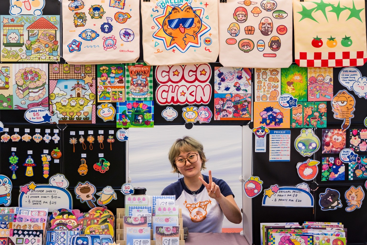 An artist posing amid colorful prints and illustrated tote bags