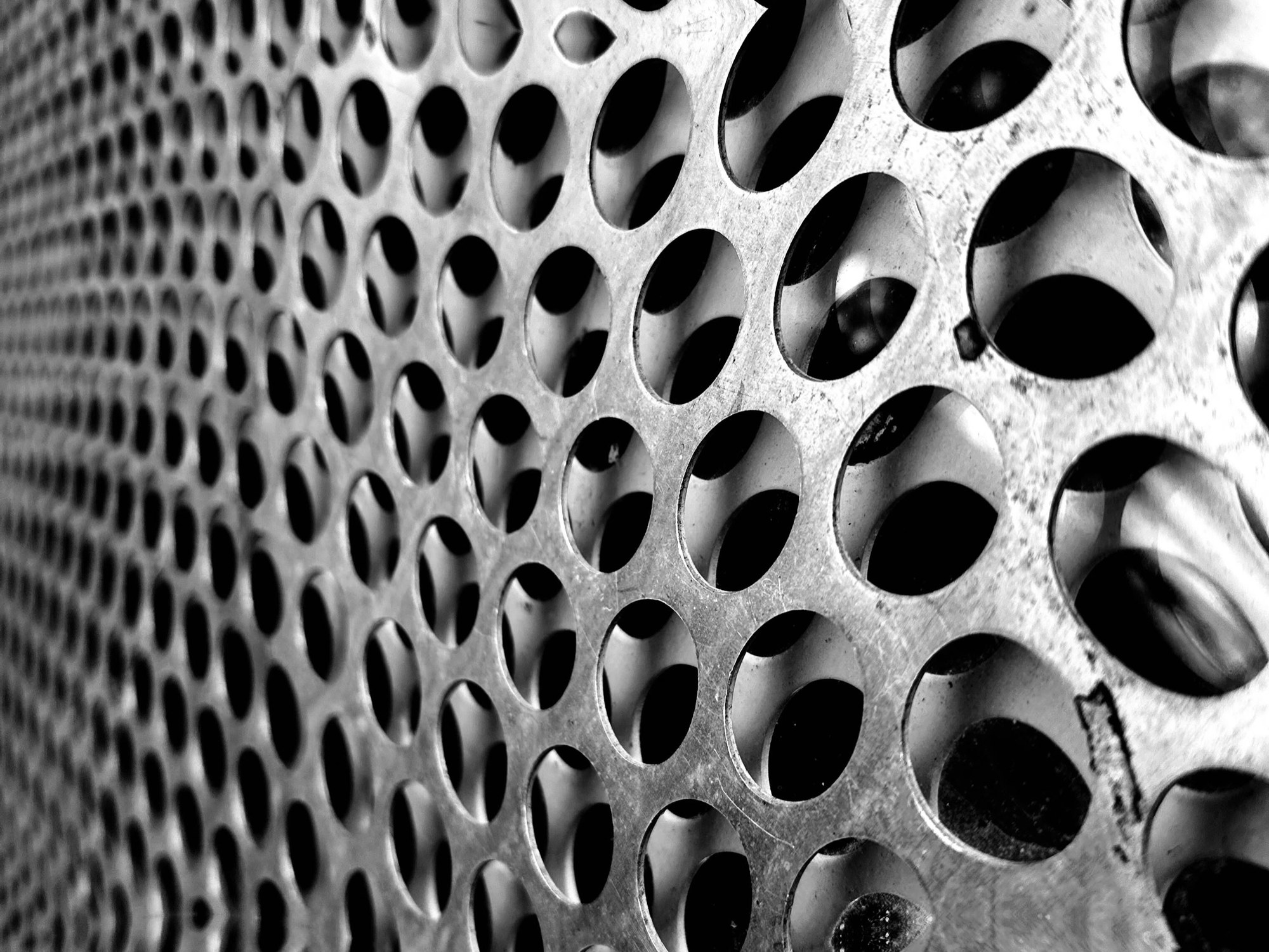 Repeating circular openings in a metal surface, photographed in black and white