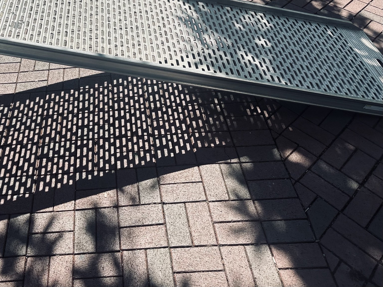 A metal bench casting patterned shadows on paving stones