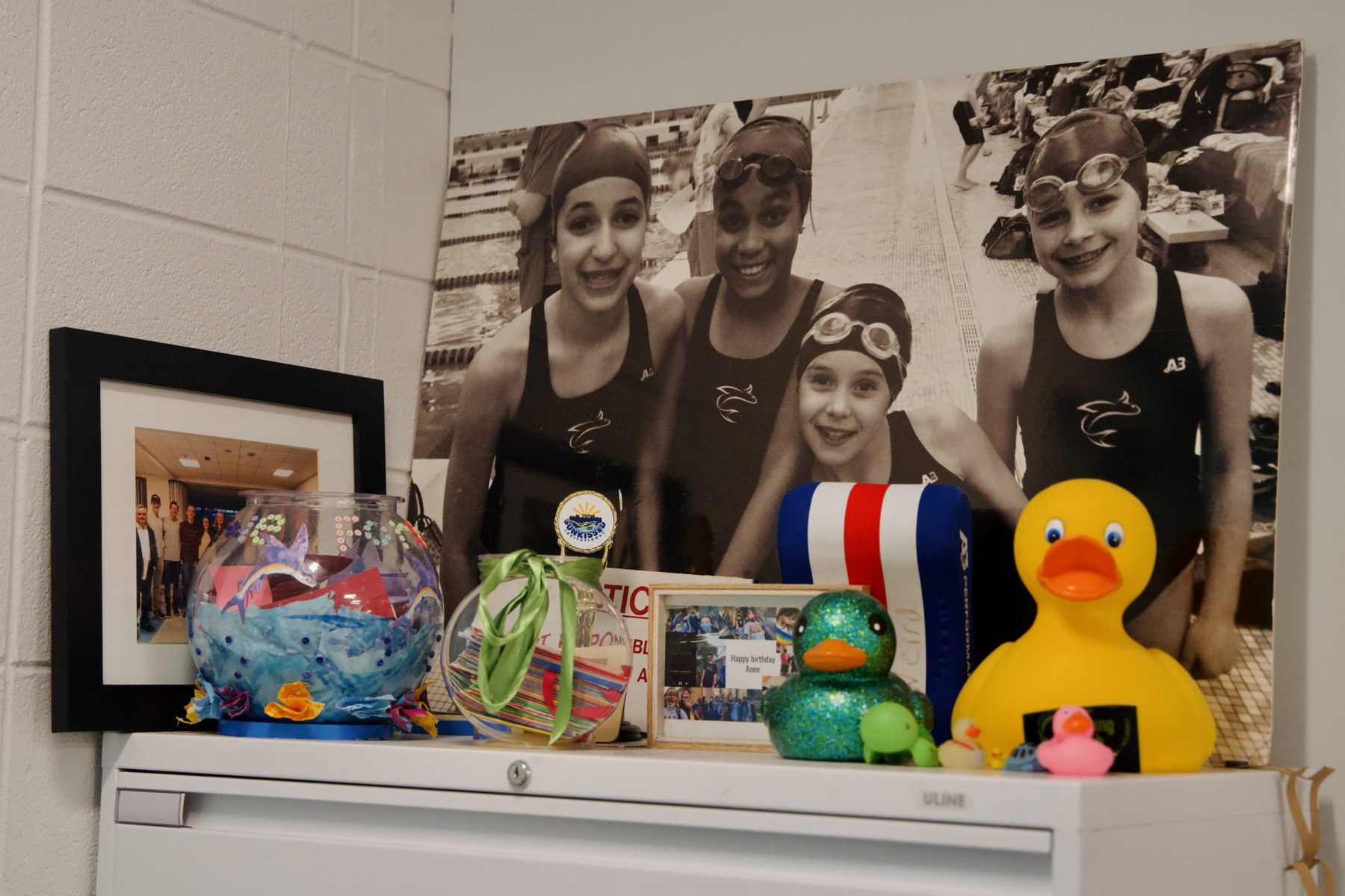 By Anne Wolff’s desk is a cabinet decorated with souvenirs given to her over the years. The girls in the picture are at a swim meet 12 years ago (From left: Eve Rubovits, Zinzi Steele, Erin Long, Quinn Sciarra). They’re in their 20s now, Wolff says.