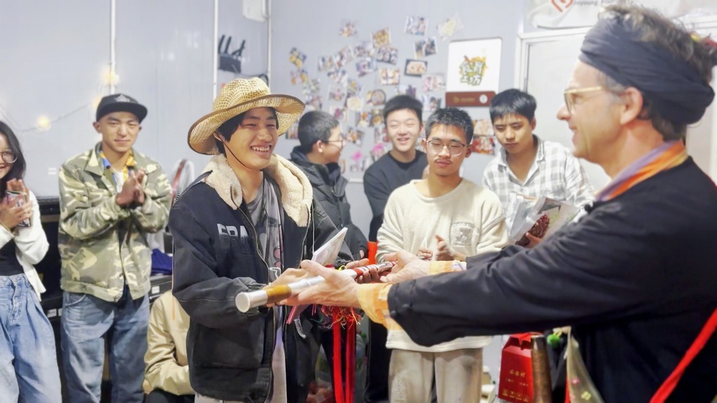 “Although we had squabbles and conflicts, I am glad you have got the nerve to step over your fear,” Lustig(right) says to Chenbang (center-left), handing him a Jingpo long sword at his surprise coming-of-age birthday party. The sword symbolizes how the youth now has the power to fight through life.