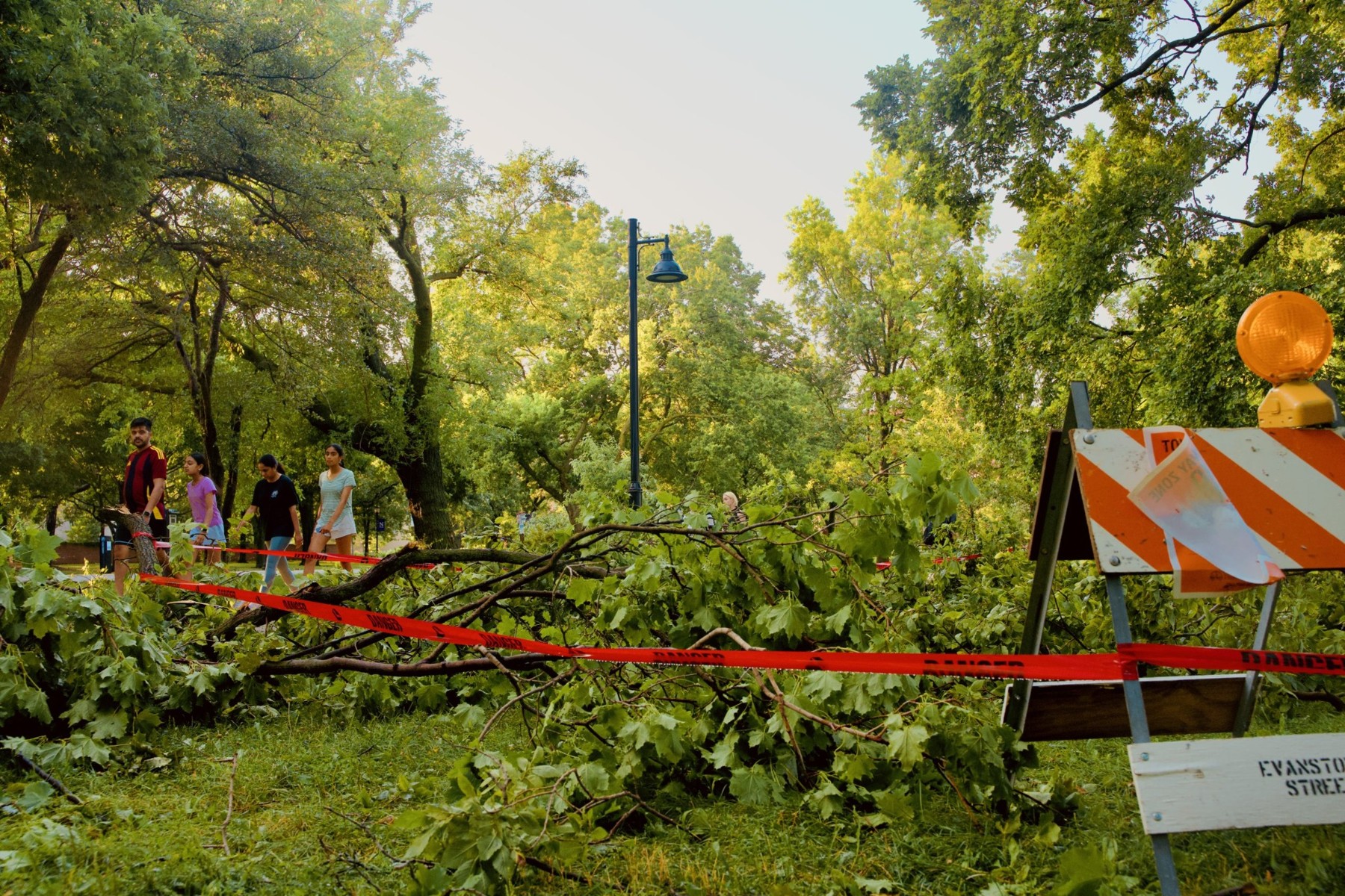 Pedestrians walk past a downed tree cordoned off with caution tape.